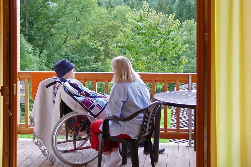 Eine Person im Rollstuhlund ein Gast sitzen auf dem Balkon der Hospiz-Gemeinschaft